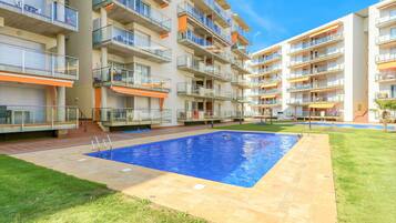 Un edificio de apartamentos moderno con varios balcones, piscina y césped bien cuidado.