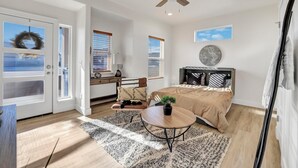 Un dormitorio con cama, escritorio, silla, ventilador de techo y vistas al exterior.