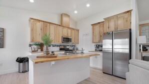 Cocina moderna con gabinetes de madera, refrigerador de acero inoxidable e isla central con pileta y microondas.