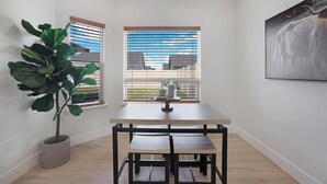 Un pequeño comedor con una mesa, sillas, una planta en maceta y una ventana con persianas.