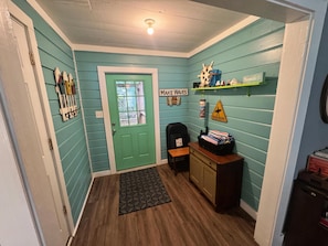 Un couloir aux murs de couleur turquoise, une porte verte, un petit bureau et une étagère contenant divers objets.