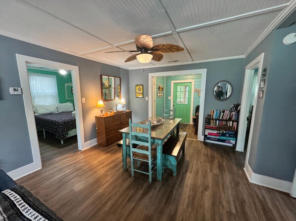 A room with a wooden floor, a dining table with chairs, a ceiling fan, a dresser, and a bookshelf. - Key Lime Lounge steps from the beach! (Folly Beach)