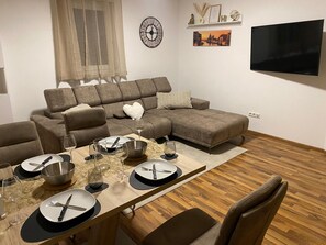 A modern living room with a sectional sofa, a dining table set for four, and a flat-screen TV mounted on the wall. - Vacation apartment Delja (Aulendorf)
