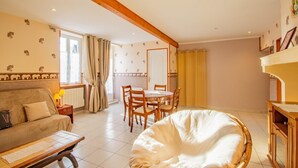 Una habitación acogedora con sofá, una mesa de comedor con sillas, un armario de madera y un gran ventanal con cortinas.
