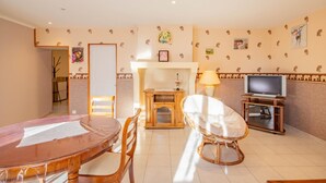Una sala de estar acogedora con una mesa de comedor de madera, una silla de mimbre, un televisor y una chimenea.