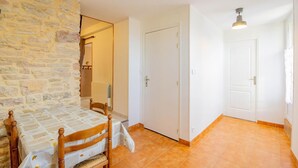 Una habitación con pared de piedra, una mesa de comedor de madera con sillas, una puerta blanca y suelo de baldosas.