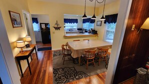 A dining area with a table and chairs, a kitchen in the background, and a view of the outside through a window with blue curtains. - 162 Peach Perfectly Located inside Lakeside! (Lakeside)
