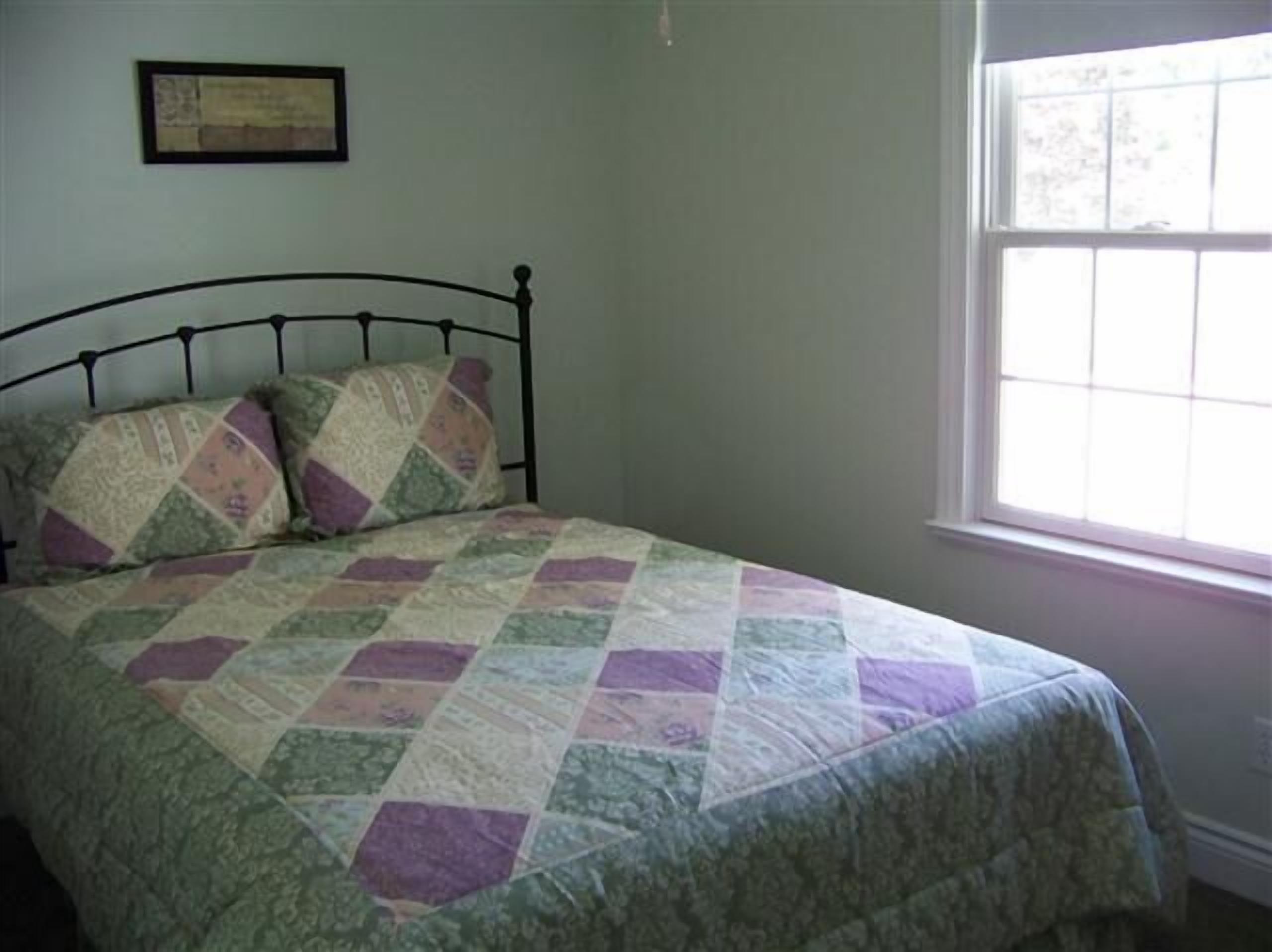 A bed with a quilt, a window, and a framed picture on the wall.