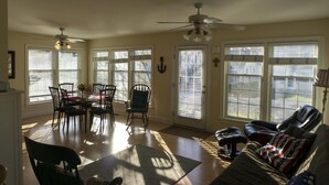 A dining area with a table and chairs, a rocking chair, a sofa with an American flag pillow, and large windows with blinds. - 533 Sycamore in Lakeside (Lakeside)