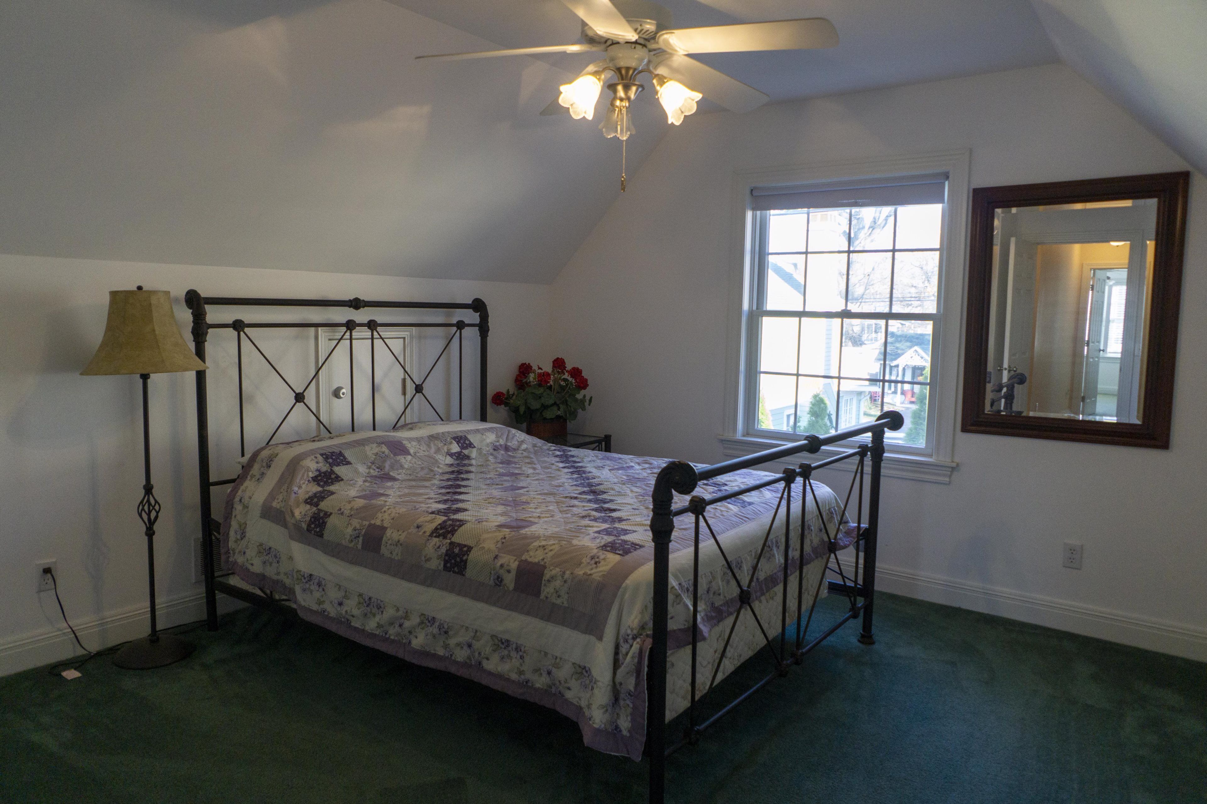 A bedroom with a bed, a ceiling fan, a window, and a mirror.