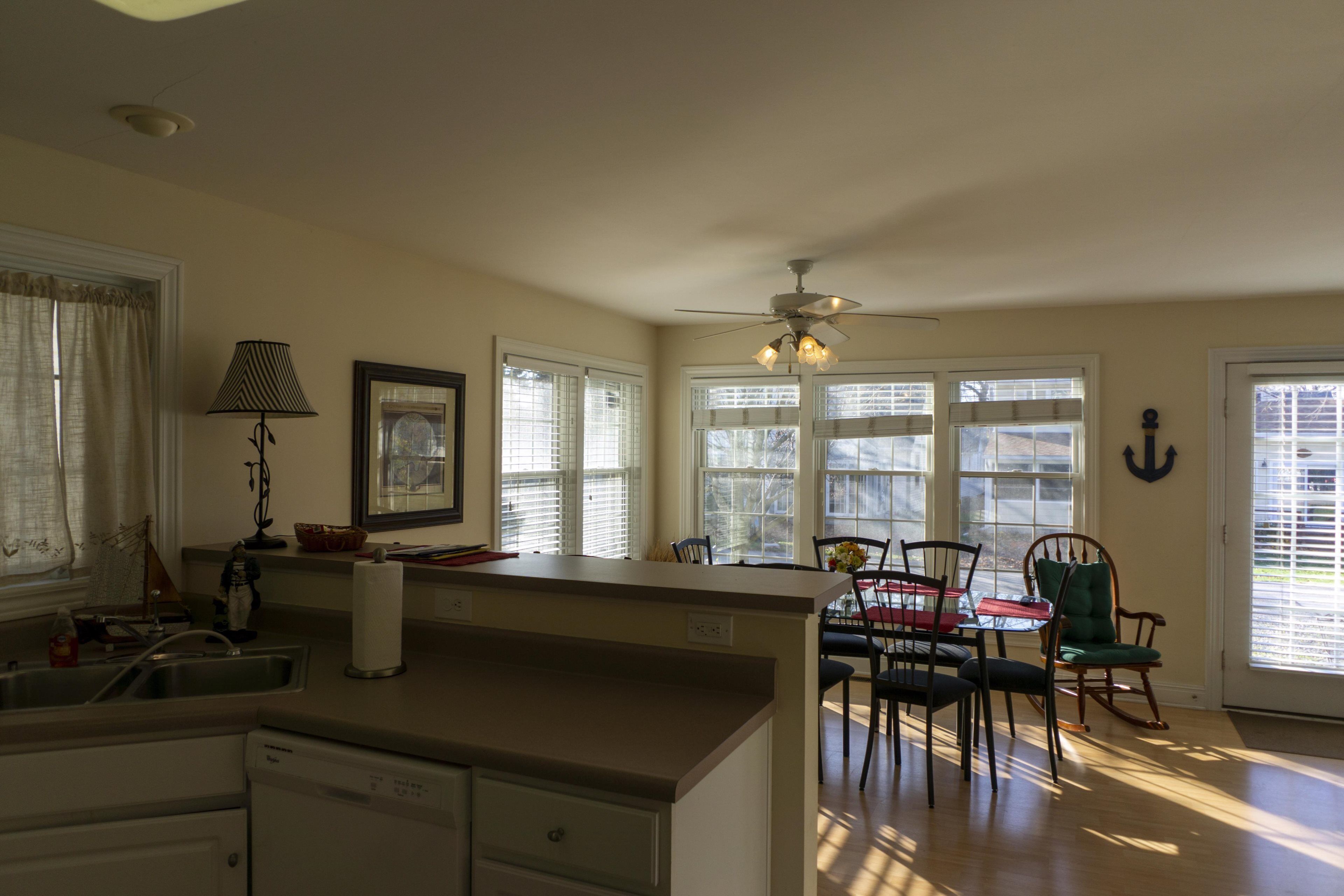 A kitchen with a dining area, large windows, and a ceiling fan.