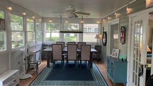 A covered dining area with a ceiling fan, wooden tables, patterned chairs, and a blue rug.