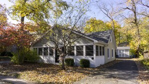 A single-story house with a front porch, a driveway, and a leaf-covered lawn.