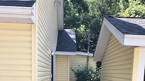 A wooden deck leading to a house with yellow siding and a black roof.