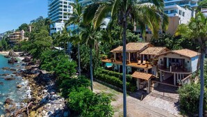 Un hotel frente al mar con vistas a la playa, varios balcones y abundante vegetación.