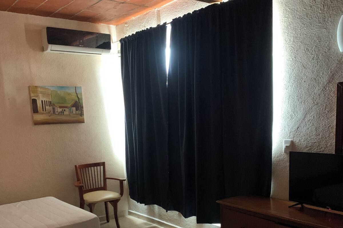 Ein Hotelzimmer mit zwei Betten, einem Holzstuhl, einem Fernseher und einem Bild an der Wand.