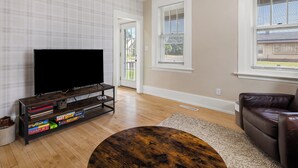 Una sala de estar con un televisor de pantalla plana sobre un soporte de madera, un sofá de cuero marrón y una mesa de centro redonda.