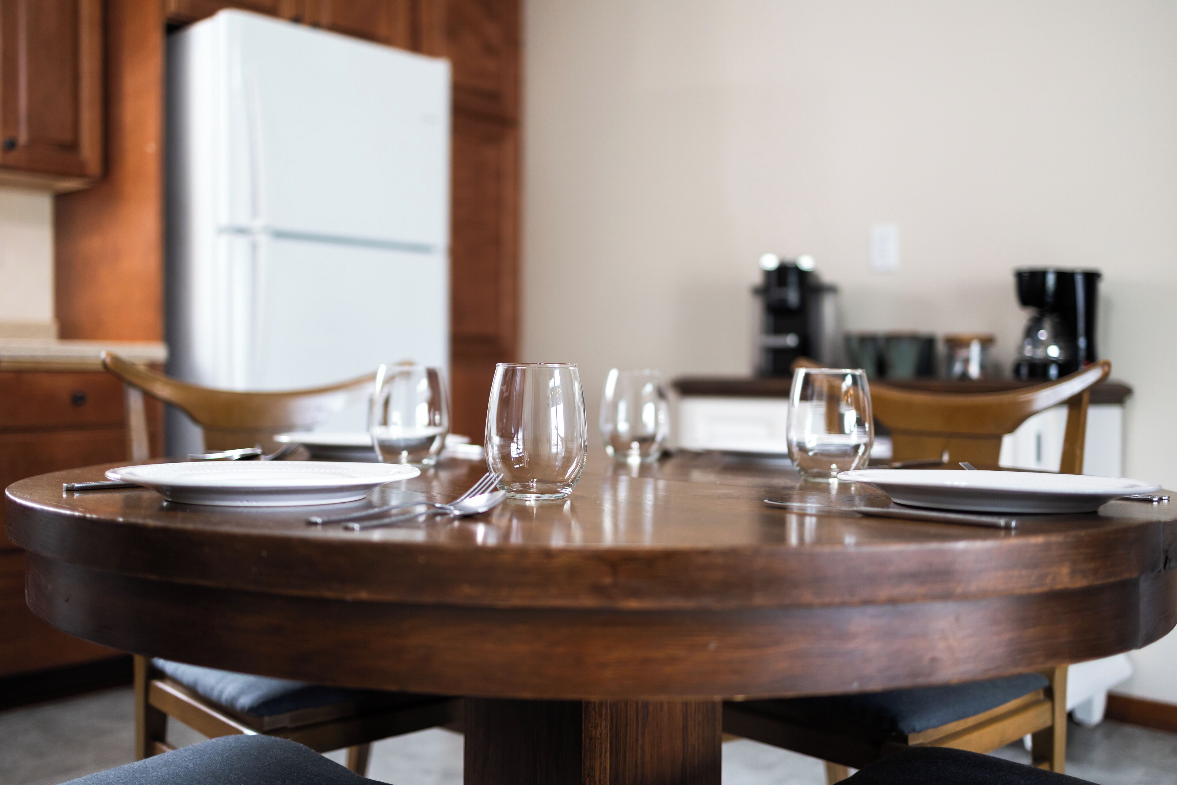 Une table de salle à manger ronde en bois, avec assiettes, couverts et verres, préparée pour quatre personnes.