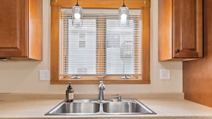 Una cocina con un lavamanos doble, armarios de madera y una ventana con persianas.