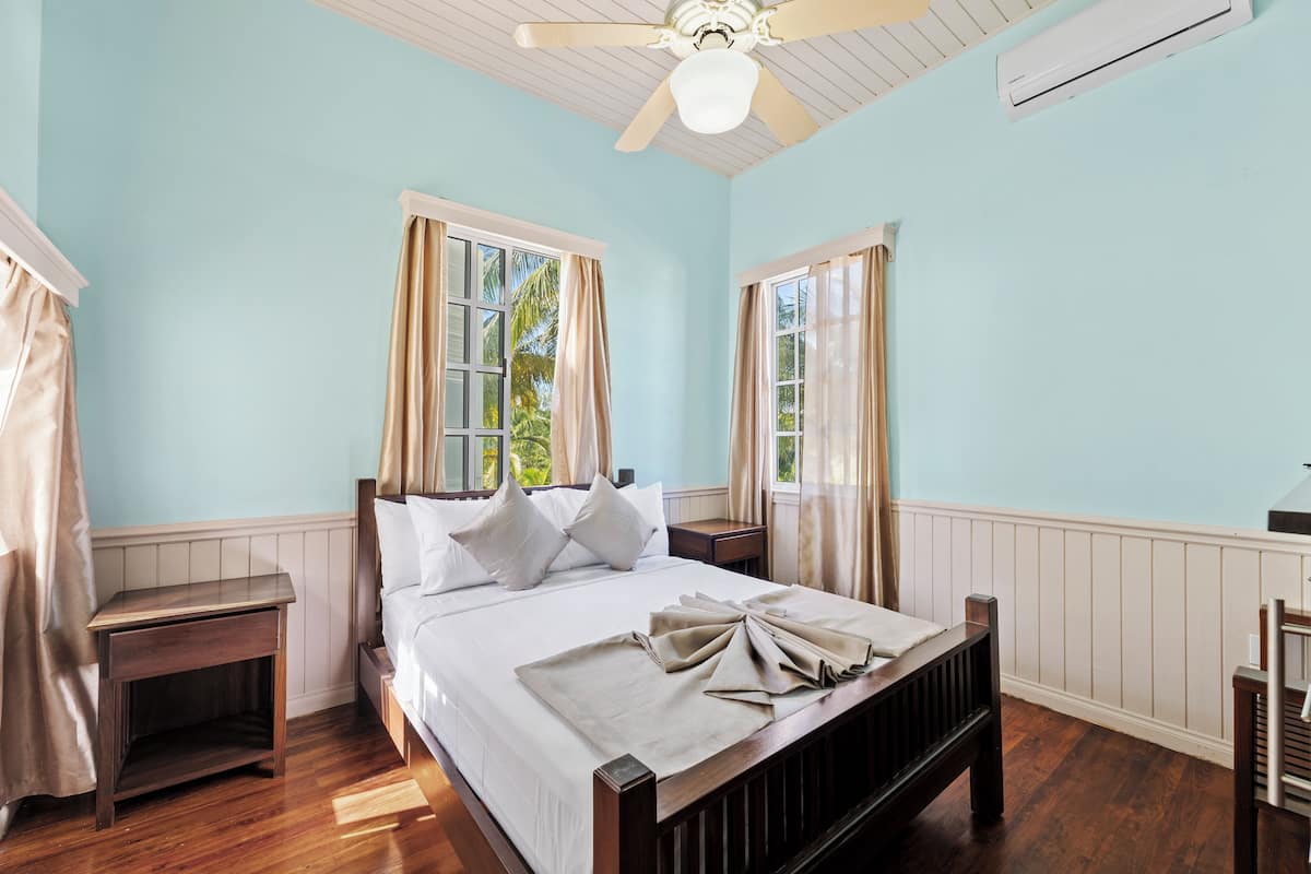 Un dormitorio con una cama de madera, dos mesitas de noche, un ventilador de techo y una ventana con cortinas.
