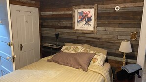Un dormitorio con pared de madera, una cama con colcha, una mesita de noche con lámpara y un cuadro enmarcado de un pez y una bandera.
