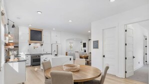 Een moderne keuken met witte kasten, een centraal eiland en een eetgedeelte met een ronde tafel en stoelen.