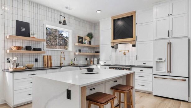 Een moderne keuken met witte kasten, een groot eiland met krukken en een ingebouwde oven.