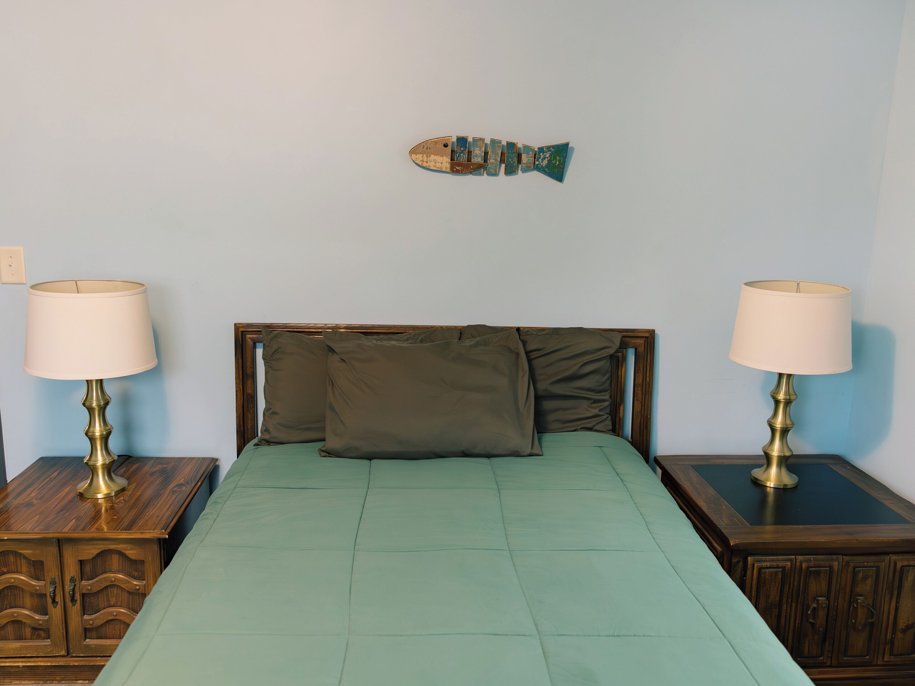 A bed with a green bedspread, two bedside tables with lamps, a wooden headboard, and a fish decoration on the wall.