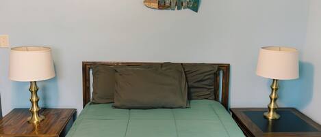 A bed with a green bedspread, two bedside tables with lamps, a wooden headboard, and a fish decoration on the wall.