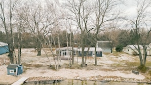 A small house surrounded by trees, a pond, and a shed. - Latitude Adjustment in Elk Rapids (Elk Rapids)