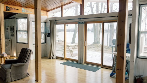 A cabin with a large sliding glass door leading to a deck, wooden floors, and a chair by the door. - Latitude Adjustment in Elk Rapids (Elk Rapids)