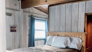 A wooden bed with a headboard, a window with curtains, and a wooden ceiling. - Latitude Adjustment in Elk Rapids (Elk Rapids)