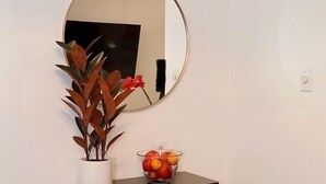 Een hoekje met een zwart console tafeltje, een potplant, een fruitschaal en een ronde spiegel aan de muur.