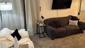 Een woonkamer met een bank, een bijzettafeltje, een lamp, een televisie en een raam met gordijnen.