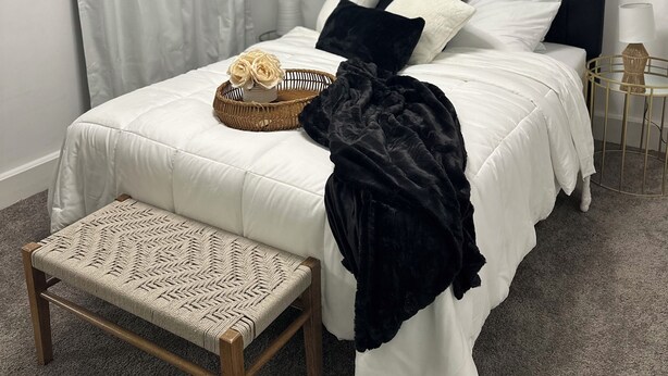 Een keurig opgemaakt slaapkamer met een bed, nachtkastje en een klein bankje.