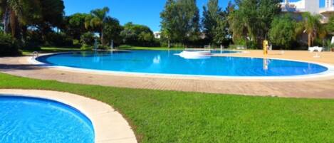 A large, circular swimming pool with a surrounding grassy area and trees.