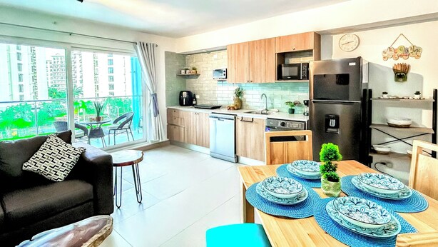 A modern apartment with a kitchen, dining area, and a balcony with a view of buildings. - Modern Paradise Relax & Explore at Viva Jaco (Jaco)