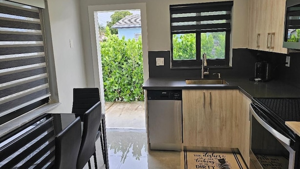 A compact kitchen with a dishwasher, wooden cabinets, a black countertop, and a window with a view of greenery. - Charming 2-bedroom apartment in terrific Hollywood with AC, WiFi (Hollywood)