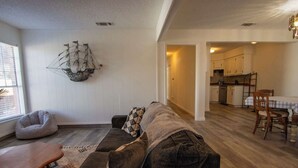 Un salon comprenant un canapé, une table basse, un élément décoratif mural et une vue sur la cuisine.