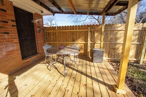 Eine Holzterrasse mit Tisch und Stühlen, eine Ziegelwand und ein Holenzaun.
