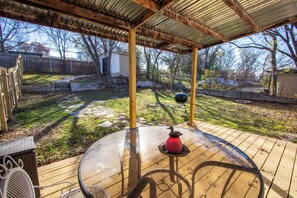 Eine überdachte Terrasse im Freien mit einem Glastisch und Stühlen, umgeben von einem Holzboden und einer Steinmauer.