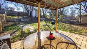 A covered outdoor patio with a glass table and chairs, surrounded by a wooden deck and a stone wall. - Spacious Stay for 16 - Central Fort Worth (Fort Worth)