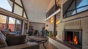 A spacious living room with a fireplace, a dining area, and a kitchen in the background.