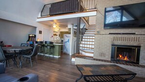 A spacious living area with a fireplace, a dining table, and a kitchen in the background.