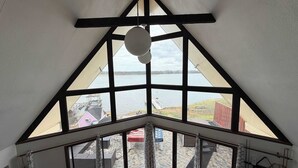 A room with a large triangular window offering a view of a lake and buildings.