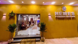 L’entrée de l’hôtel Nemes Pyramids View Inn se distingue par sa porte en verre, ses murs jaunes et ses deux plantes en pot.