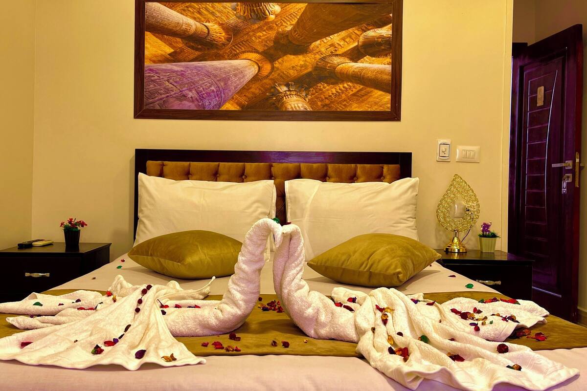 A hotel room with a bed, pillows, a nightstand, a lamp, and a painting on the wall.