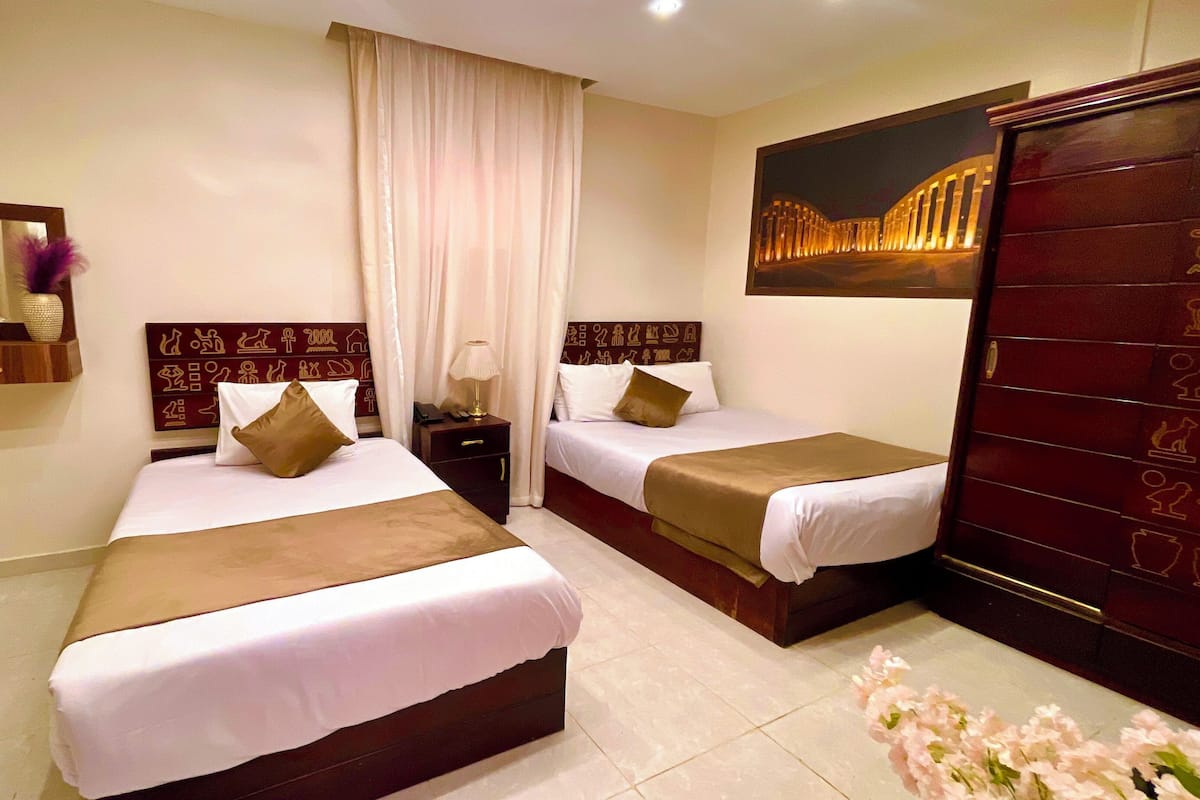 A hotel room with two beds, a nightstand, a mirror, a wall-mounted artwork, and a wardrobe.