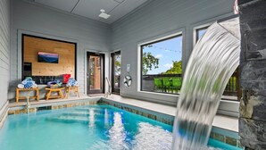 A swimming pool with a waterfall feature, wooden deck chairs, and a view of the outdoors. - Lakefront home with retro accents, private pool, and private dock. (Sevierville)