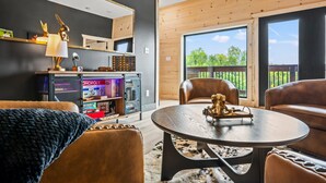 A modern living room with a round table, leather sofas, a bookshelf, and a large window offering a view of the outdoors. - Lakefront home with retro accents, private pool, and private dock. (Sevierville)